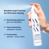 Hand holding a bottle of Color Wow Get in Shape hairspray with text about its formula on a blue background: Breakthrough formula for effortless styling. Elasticising polymers give hair flexibility, heat protectants safeguard strands, humectants hydrate + boost shine.
